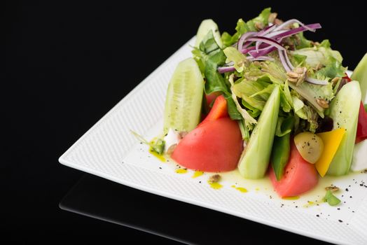 vegetable salad in a square plate on a black background, isolated