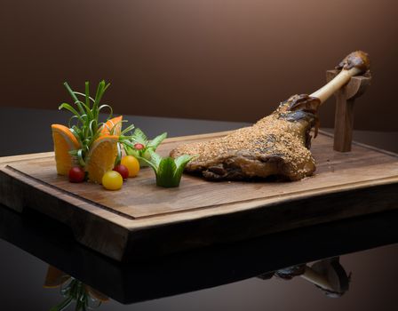 roasted meat with sesame seeds on a wooden tray, on a dark background