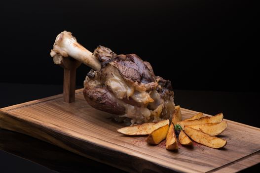 roast meat with bone on a wooden tray, dark background, isolated