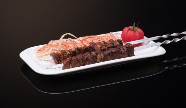 kebab sticks on skewers with onion and tomato on dark background