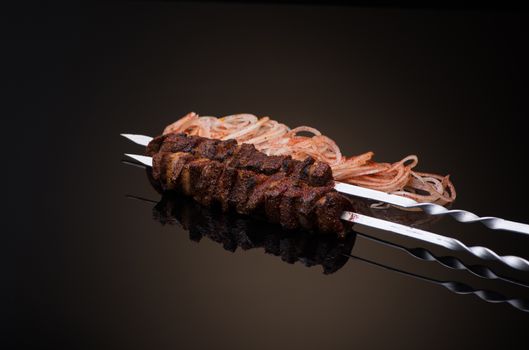 kebab sticks on skewers with onion and tomato on dark background