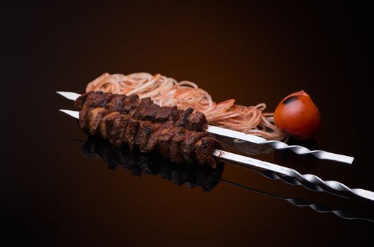 kebab sticks on skewers with onion and tomato on dark background