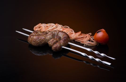 kebab sticks on skewers with onion and tomato on dark background