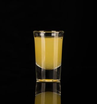 yellow alcoholic liquor in a shot glass isolated on dark background