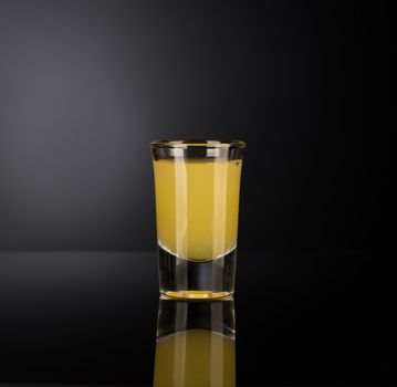 yellow alcoholic liquor in a shot glass isolated on dark background with backlight