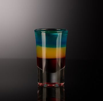 mixed alcoholic liquor in a shot glass isolated on a dark background with backlighting