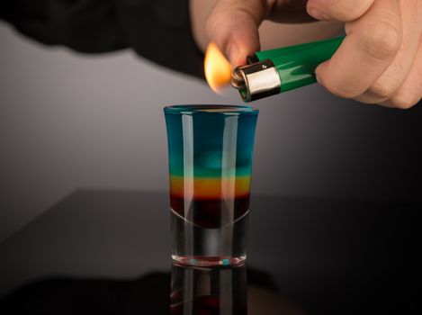 bartender sets fire to a mixed alcoholic cocktail in a shot glass, close-up