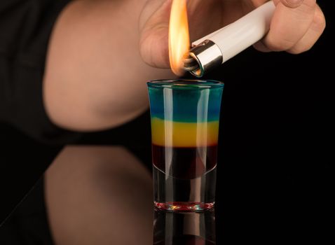 bartender sets fire to a mixed alcoholic cocktail in a shot glass, close-up