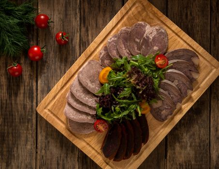 sliced smoked meat on a cutting board decorated with vegetables, top view