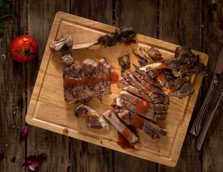 sliced roasted meat on a wooden surface and dressed with sauce, top view