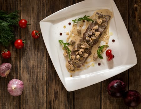 a dish of meat and mushrooms seasoned with gravy on a square plate, top view