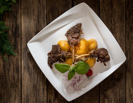 a dish of meat and potatoes in a plate on wooden background, top view