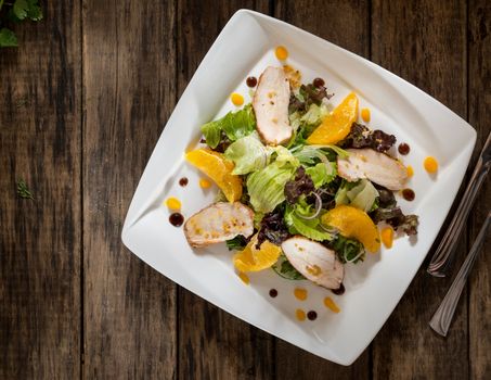 dish of chicken and salad in a white square plate on wooden boards, top view