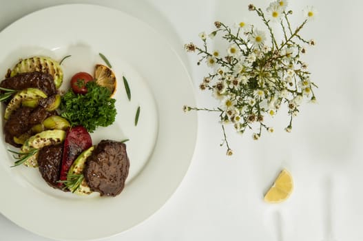 roast meat with lemon slices on a white surface with a shadow from the wine glasses