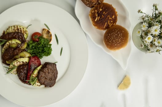 roast meat with lemon slices on a white surface with a shadow from the wine glasses