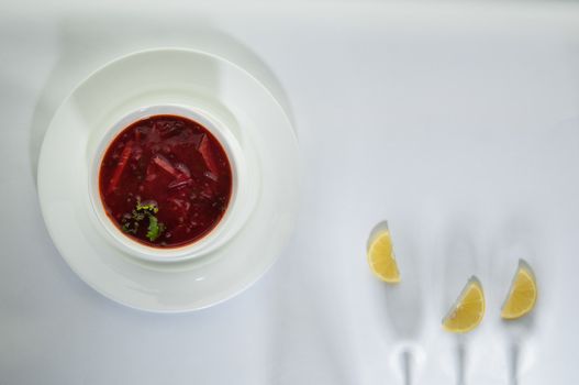 soup in a plate with lemon slices on a white surface with a shadow from the wine glasses