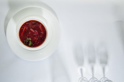 soup in a plate on a white surface with a shadow from the wine glasses