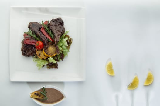 roast meat with lemon slices on a white surface with a shadow from the wine glasses