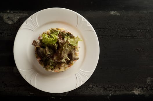 salad olivier in a white plate on a wooden old surface. Olivier salad with greens in a round plate on a wooden old board