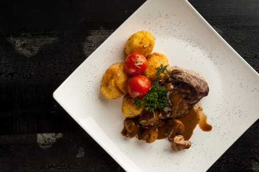 meat dish on a wooden old surface. fried meat with potatoes in a white plate on a wooden old board