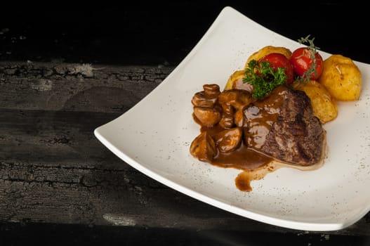 meat dish on a wooden old surface. fried meat with potatoes in a white plate on a wooden old board