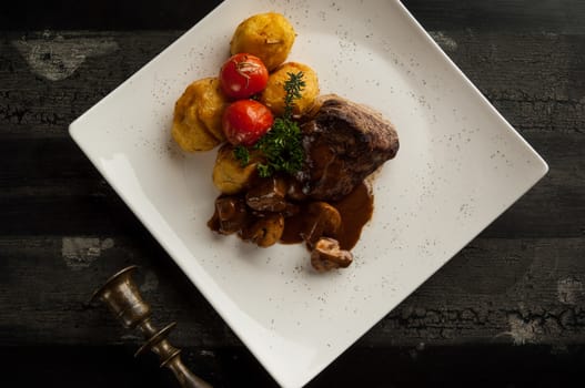 meat dish on a wooden old surface. fried meat with potatoes in a white plate on a wooden old board