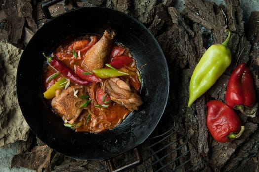 chicken dish with vegetables in a frying pan on the background of tree bark