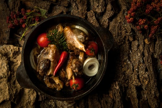 chicken dish with vegetables in a frying pan on the background of tree bark