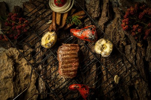 a piece of roasted meat with vegetables on the grill on a background of tree bark