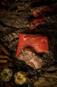 piece of raw meat with vegetables on the grill on a background of tree bark