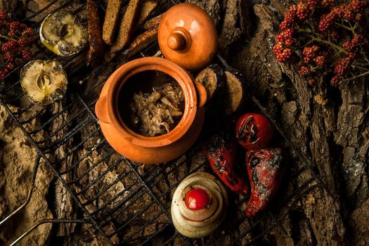 vegetarian dish in a clay pot with roasted vegetables on the grill on a background of tree bark