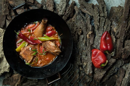 chicken dish with vegetables in a frying pan on the background of tree bark