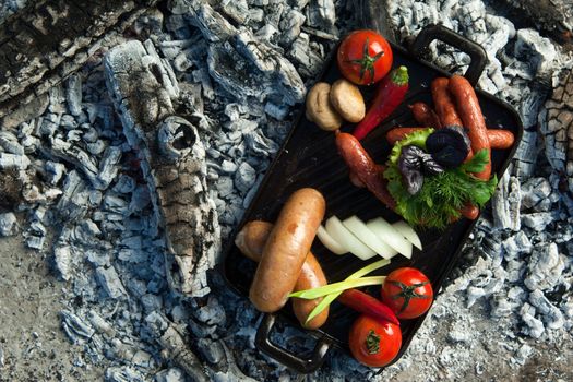 smoked sausages and tomatoes lie on charcoal. the dish is cooked and smoked on charcoal