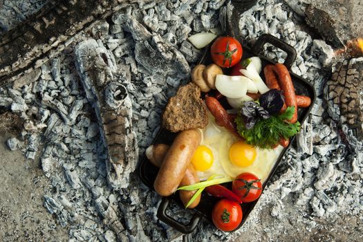 smoked sausages with tomatoes and eggs lie on charcoal. the dish is cooked and smoked on charcoal