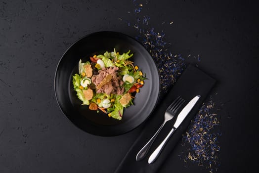 a dish of boiled meat on a black wooden surface, top view