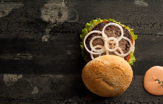 cheeseburger on an old wooden surface of dark color. hamburger with sauce and ketchup on an old wooden surface of dark color