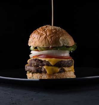 juicy cheeseburger on a plate on a black background, close - up