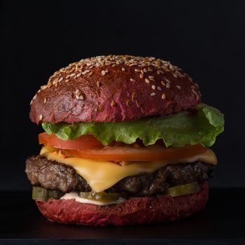 juicy cheeseburger of red bread on a black background, close-up