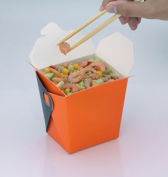 chinese food to takeaway. shrimp with vegetables in a cardboard box on a light background. takes chinese food with chopsticks