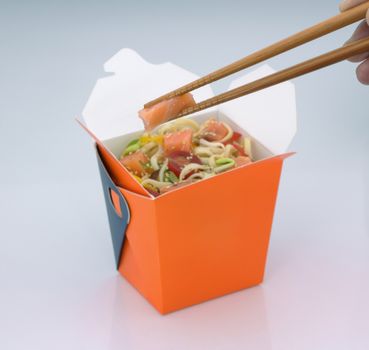 chinese food to takeaway. noodles with meat and vegetables in a cardboard box on a light background. takes chinese food with chopsticks