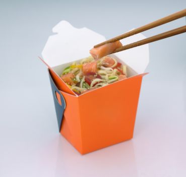 chinese food to takeaway. noodles with meat and vegetables in a cardboard box on a light background. takes chinese food with chopsticks