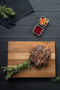 grilled meat with greens and sauce on a cutting board on a black wooden background