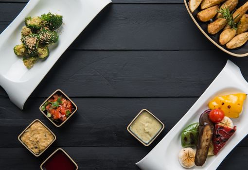 salads, vegetable food and gravy in plates on a black wooden background