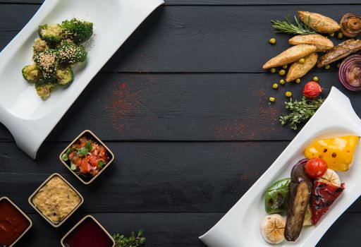 salads, vegetable food and gravy in plates on a black wooden background