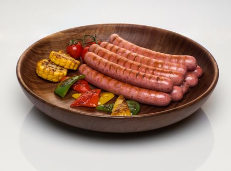 fried sausages with vegetables in a wooden plate, isolated on a white background