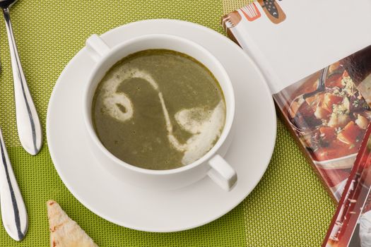 soup in a white bowl with a book and cutlery on a green tablecloth