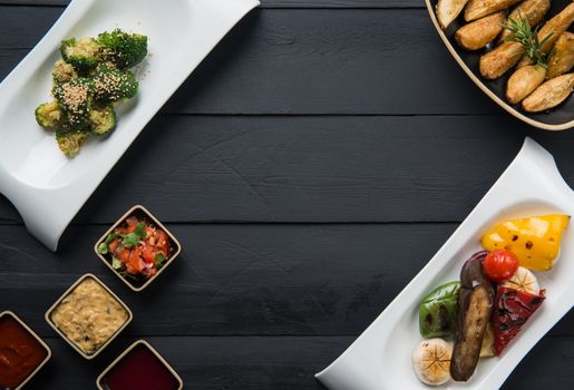 salads, vegetable food and gravy in plates on a black wooden background