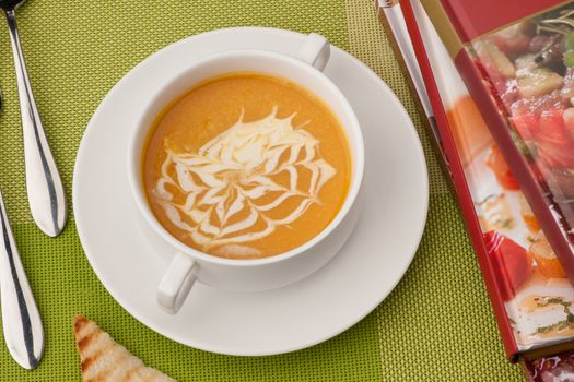 soup in a white bowl with a book and cutlery on a green tablecloth