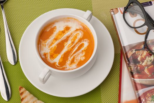 soup in a white bowl with book and glasses on a green tablecloth