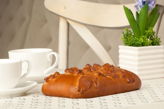 Pie and two cups of coffee on a table with flowers on the background of the chair